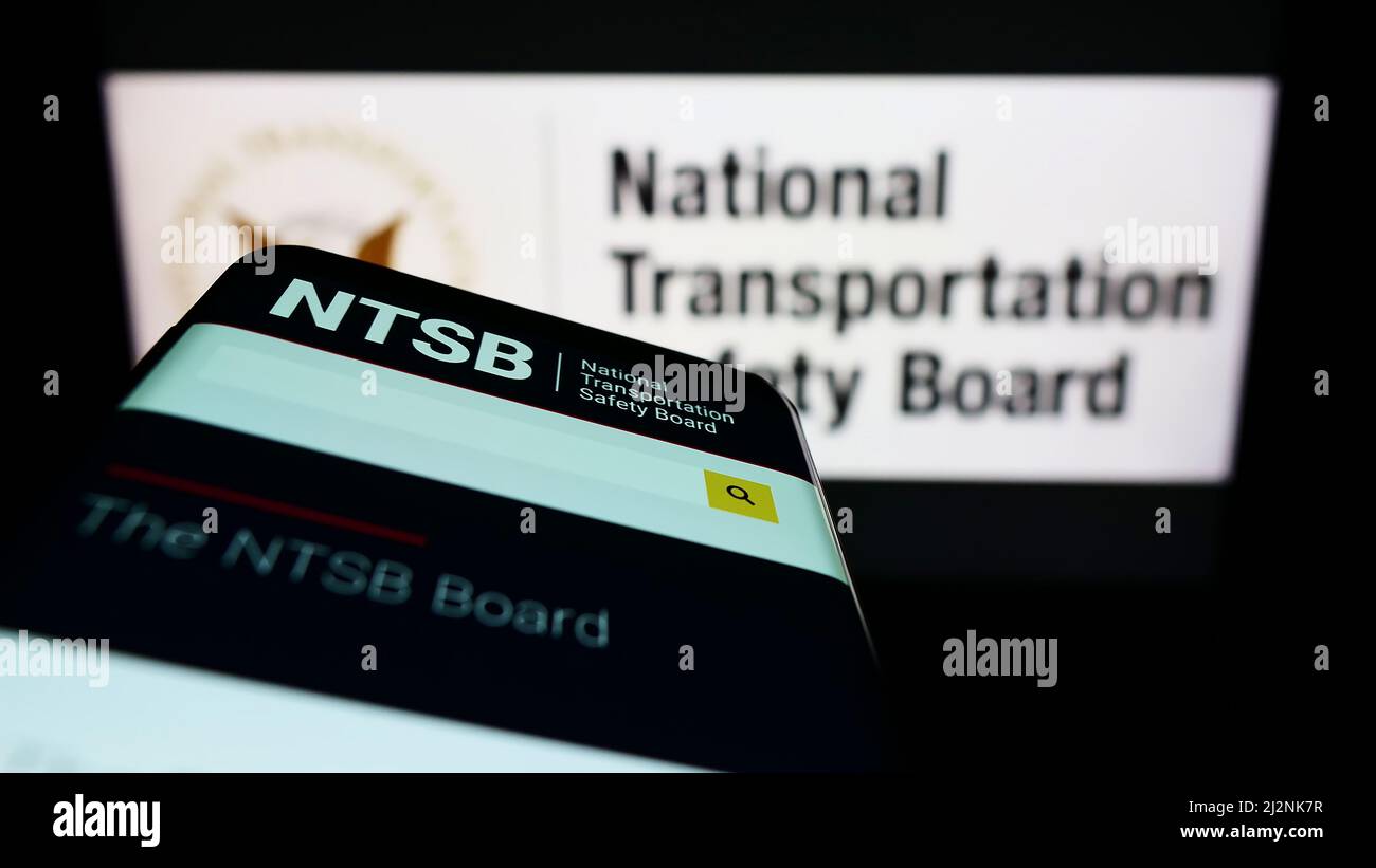Mobile phone with website of US National Transportation Safety Board (NTSB) on screen in front of seal. Focus on top-left of phone display. Stock Photo