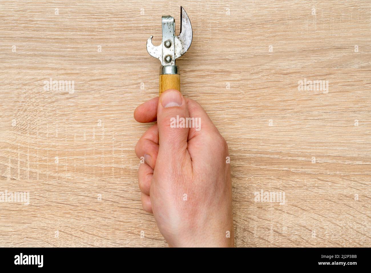 Men hand holds old can opener with wood handle Stock Photo