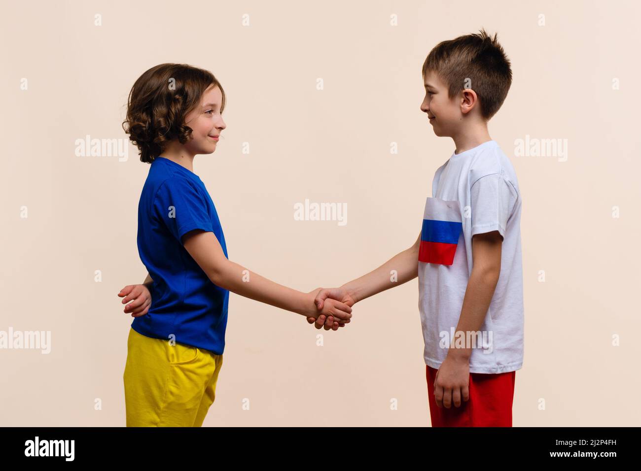 Boy and Girl in Outfits in Colors Flags Russia and Ukraine Look each Other and Make Handshake. Reconciliation, end conflict and stop war. Friendship of Fraternal Peoples. Cousins want peace Stock Photo