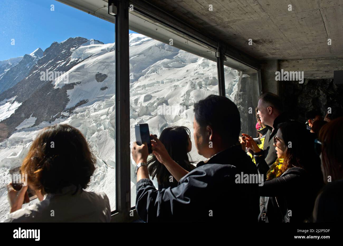 Tourists look through a glass window at the icefalls of the Eiger Glacier at the Eigerwand station of the Jungfrau Railway, Grindelwald,Switzerland Stock Photo