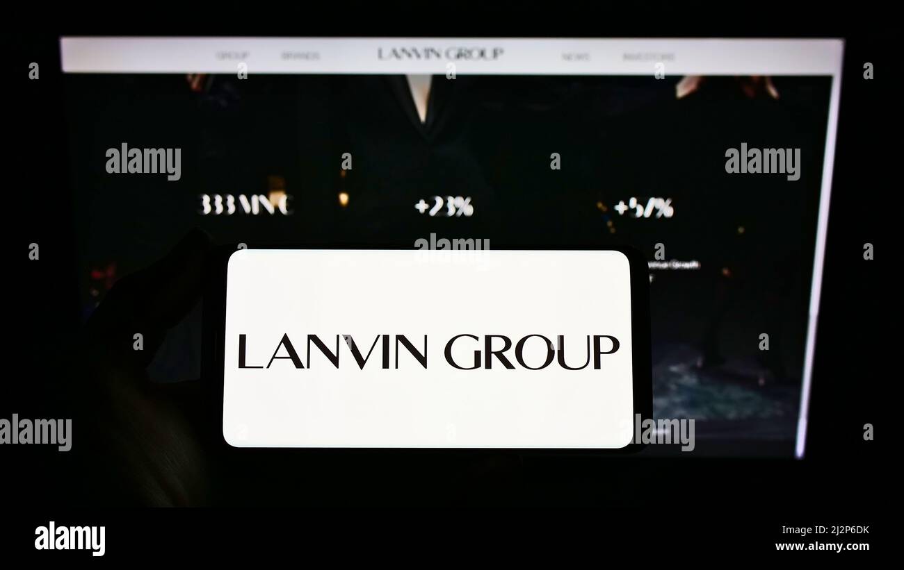 Person holding smartphone with logo of Chinese fashion company Lanvin Group on screen in front of website. Focus on phone display. Stock Photo