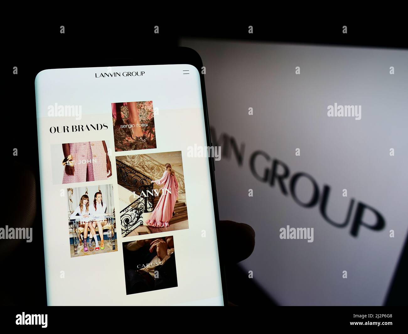Person holding cellphone with webpage of Chinese fashion company Lanvin Group on screen in front of logo. Focus on center of phone display. Stock Photo