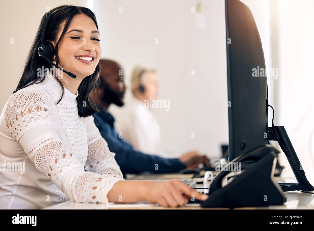 Ill call the customer right away to deliver the good news. Shot of a young call centre agent using a telephone while working on a computer in an Stock Photo