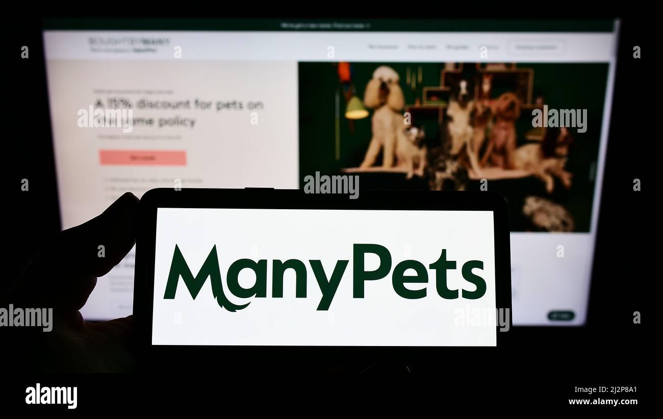 Person holding smartphone with logo of insurance company Bought By Many Ltd. (ManyPets) on screen in front of website. Focus on phone display. Stock Photo