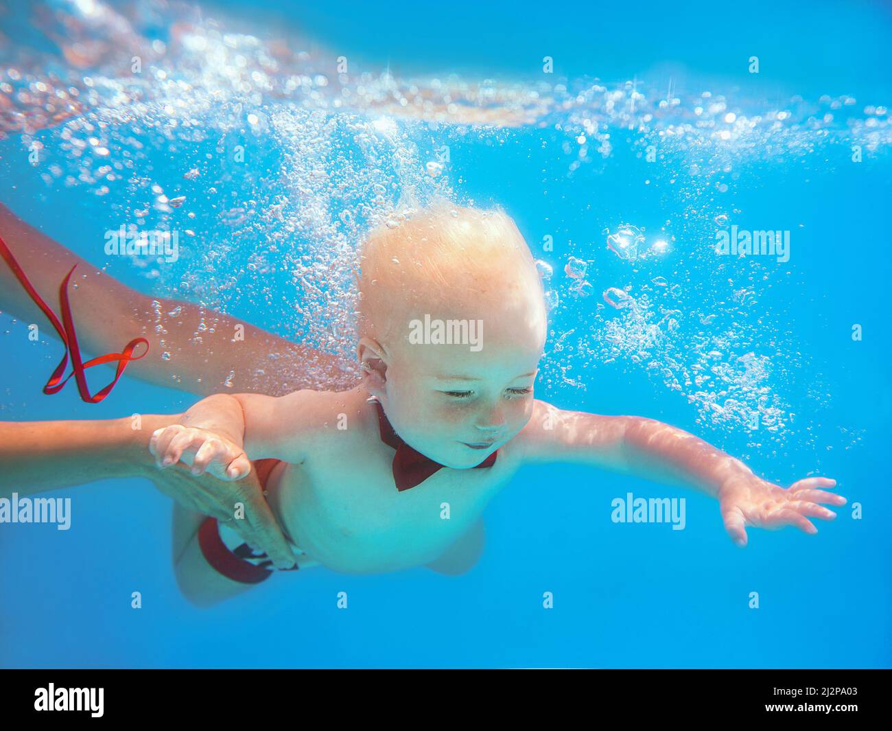 Little boy infant with red butterfly diving underwater in swimming pool