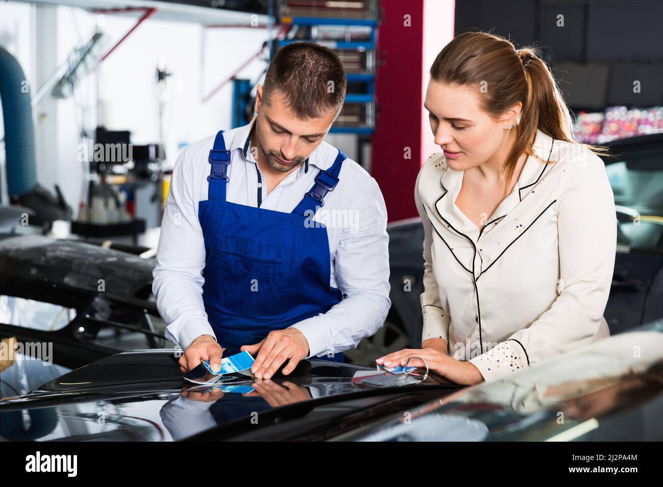 Serious car painter discussing with female client, picking up color of paint in auto repair shop Stock Photo