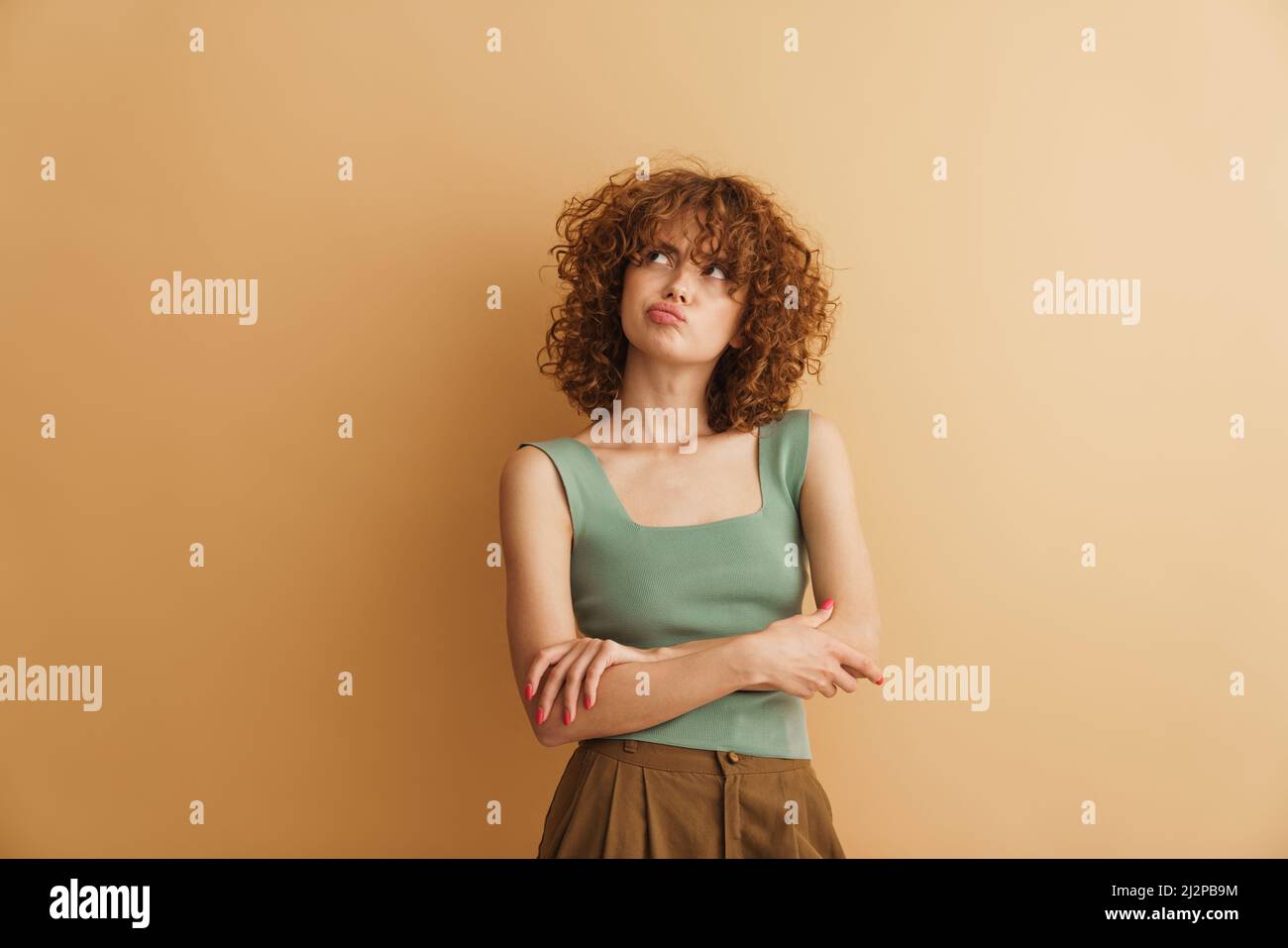 Young ginger curly woman frowning while looking upward isolated over ...