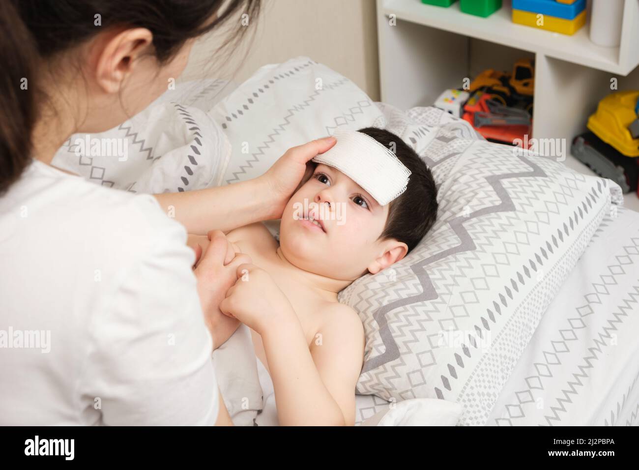 The mother cares for the feverish 4-year-old son, the child has a cooling compress on the forehead. Stock Photo