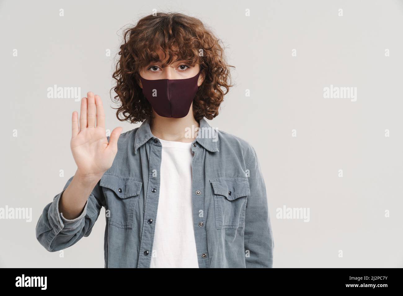 Young ginger woman in face mask showing stop gesture isolated over ...