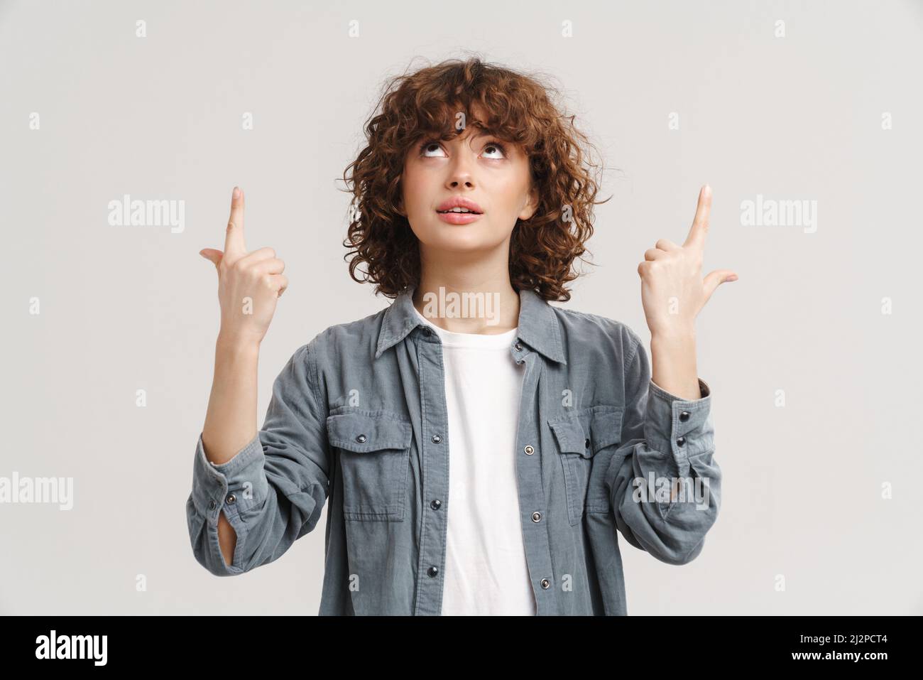 Young ginger woman in shirt pointing fingers and looking upward ...