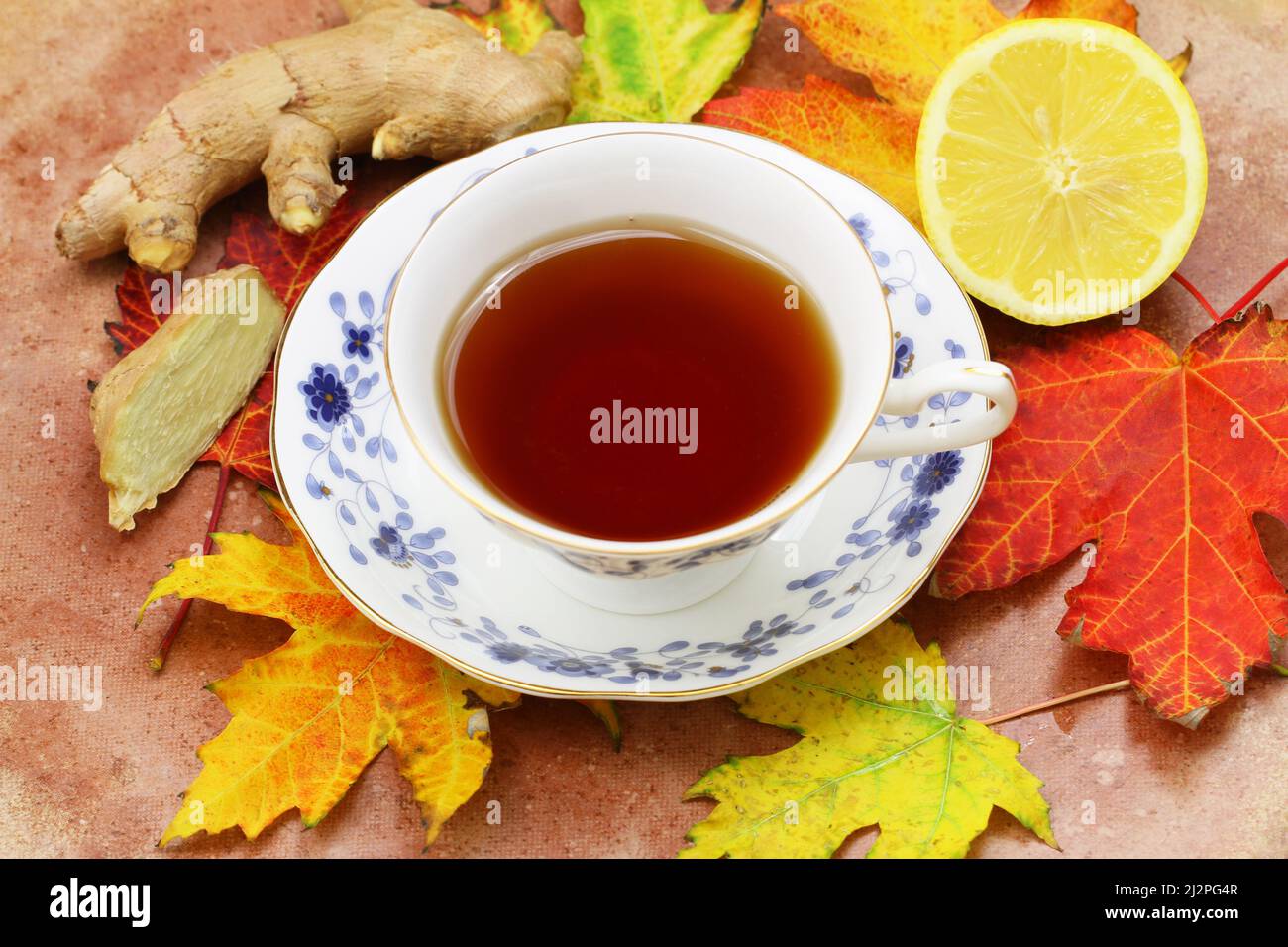 Black tea in vintage cup, lemon and fresh ginger on top of colorful autumn maple leaves on rustic wooden surface Stock Photo