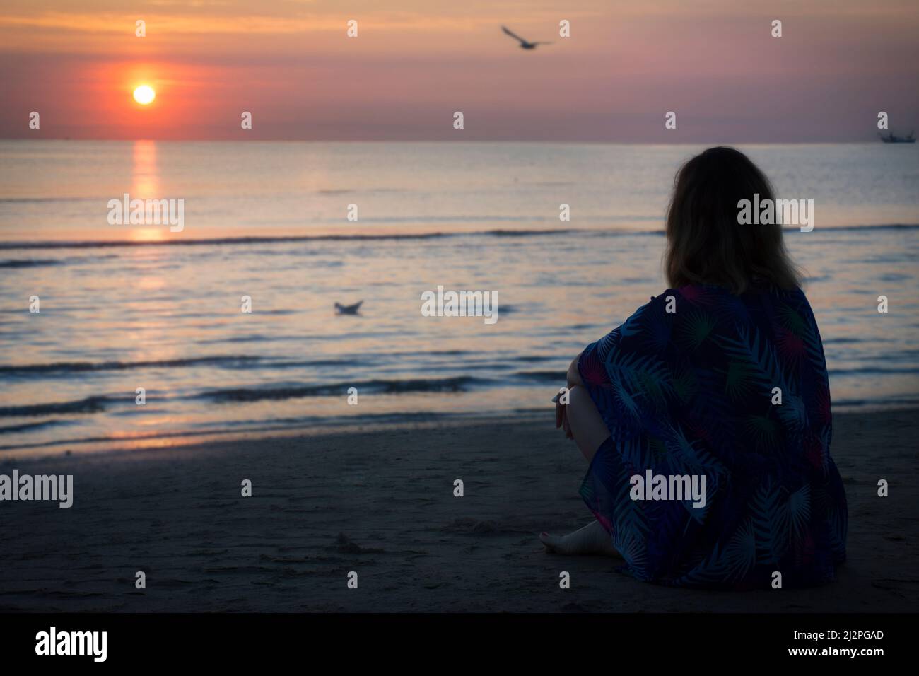 a woman is sitting on the beach and looking at sunrise in the sea Stock ...
