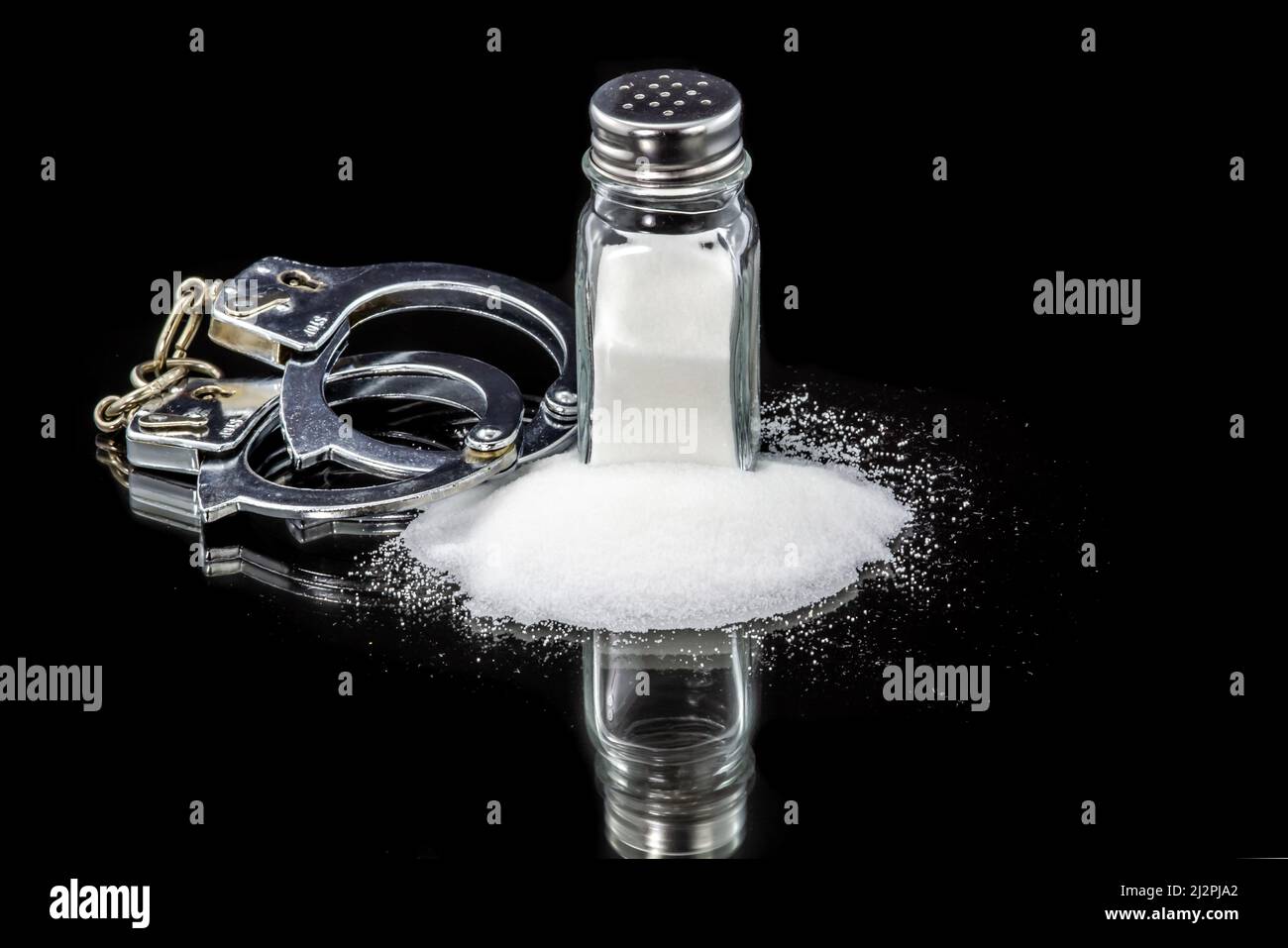 Salt shaker with spill table salt and handcuffs. Prisoner of salt concept. Stock Photo
