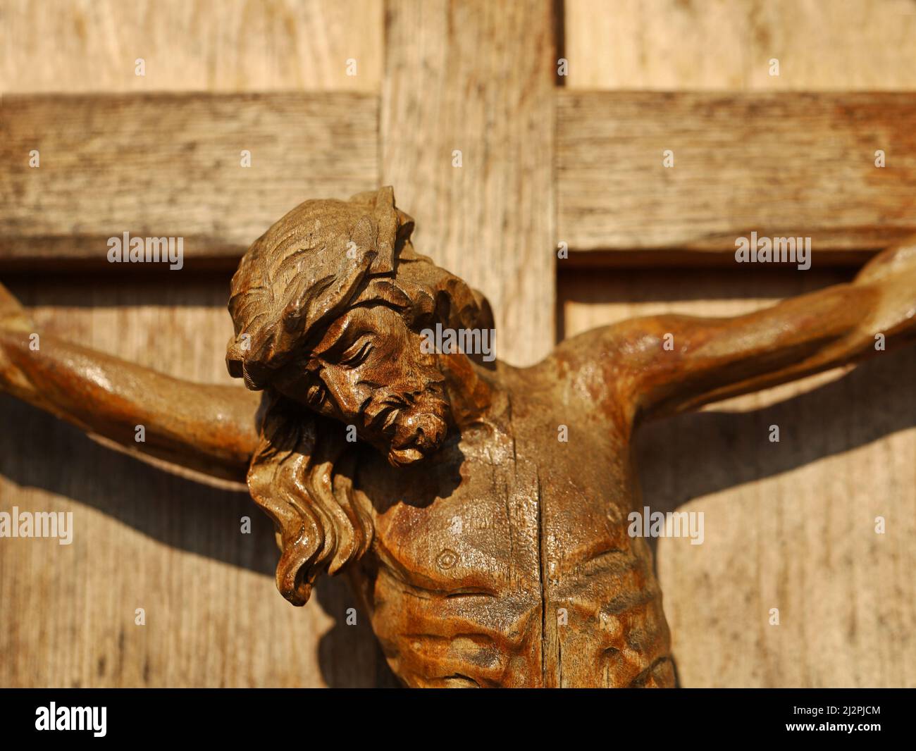 Close up of an old wooden crucifix, face of Jesus Christ on wooden cross in sunlight Stock Photo