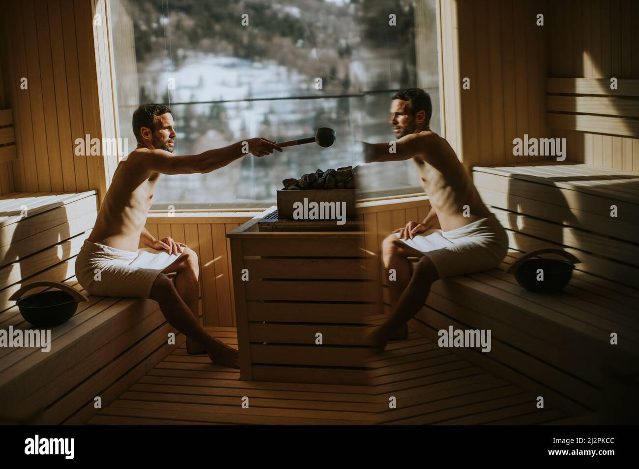 Handsome young man pouring water onto hot stone in the sauna Stock Photo -  Alamy