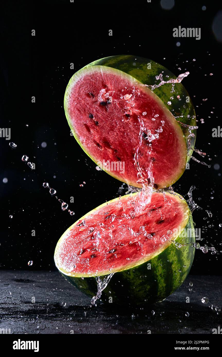 Ripe watermelon cut in half with water splash flying in the air Stock Photo
