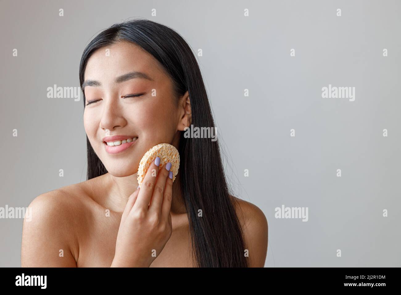 Joyful Asian woman cleaning face with cosmetic sponge Stock Photo