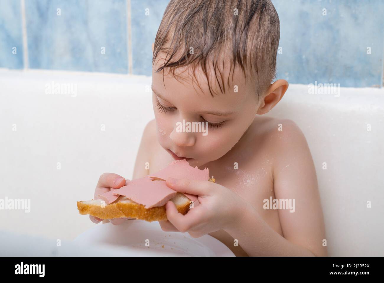 A young boy is eating in the bath. Snack in the bathroom Stock Photo ...