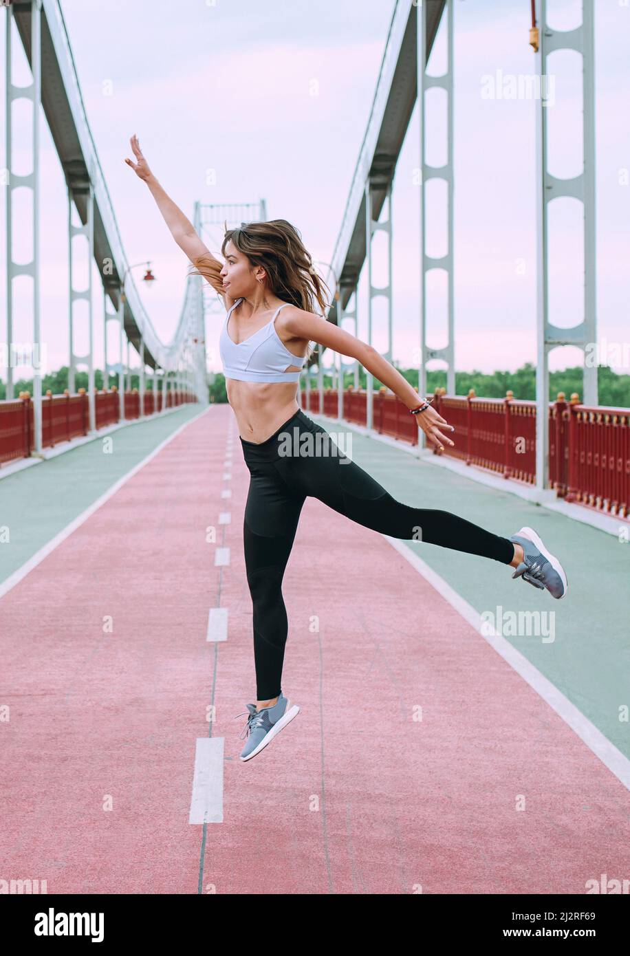 beautiful, sporty, fit, young Caucasian woman in sportswear and sneakers jumping on the bridge. Sport, activity, urban lifestyle concept Stock Photo