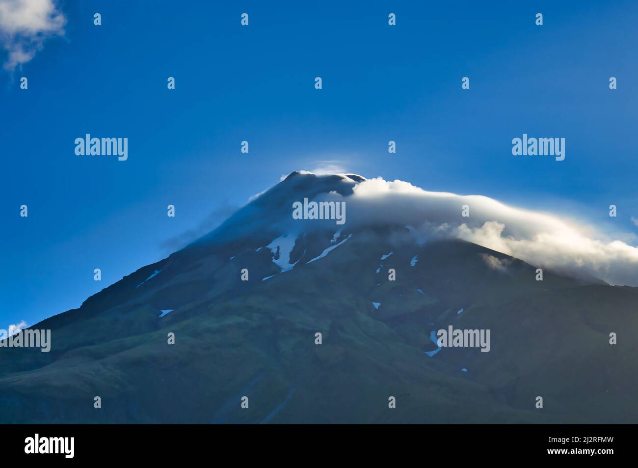 Volcano with snowfields and clouds around the summit, lit by the evening sun. Mount Taranaki (Mount Egmont), North Island, New Zealand. Stock Photo
