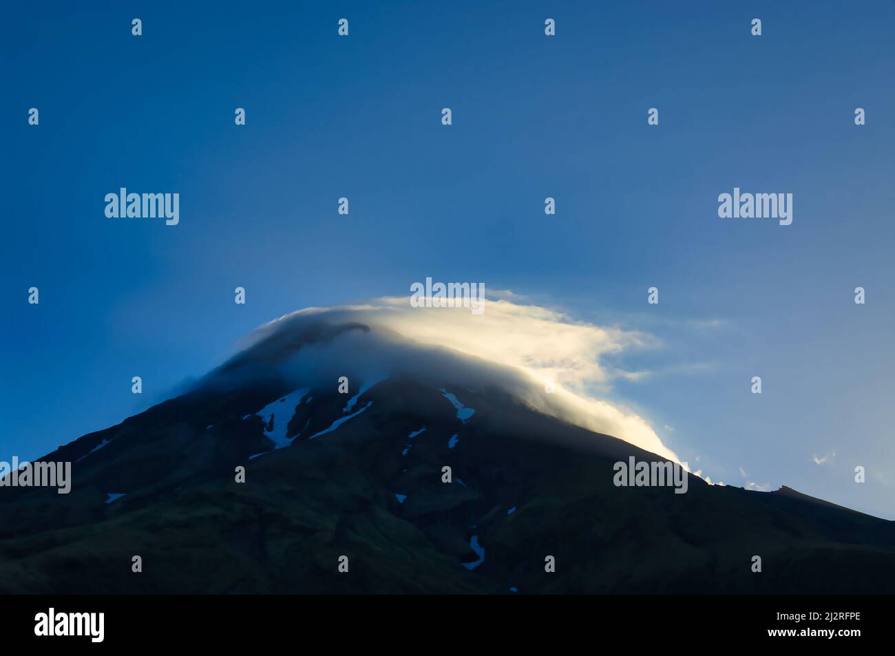 Volcano with snowfields and clouds around the summit, lit by the evening sun. Mount Taranaki (Mount Egmont), North Island, New Zealand. Stock Photo