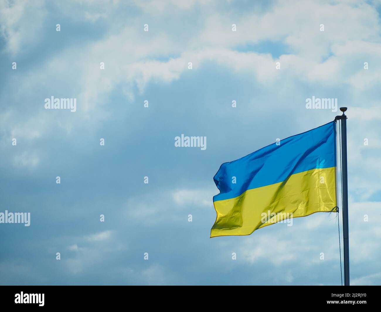 The flag of Ukraine flys against a cloudy blue sky in solidarity with the people of Ukraine. Stock Photo