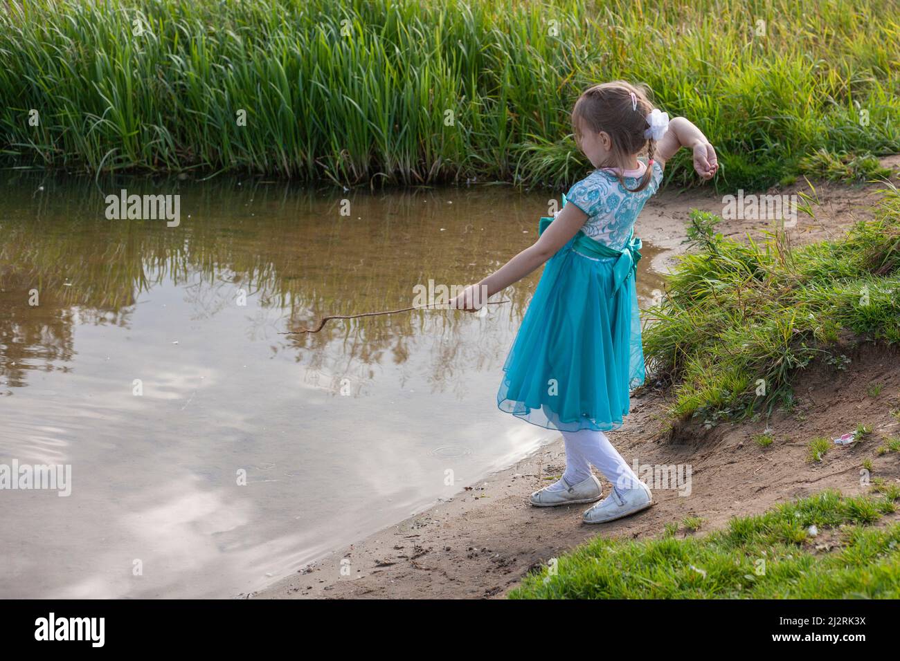 A girl in a blue dress throws pebbles into the water. A child plays