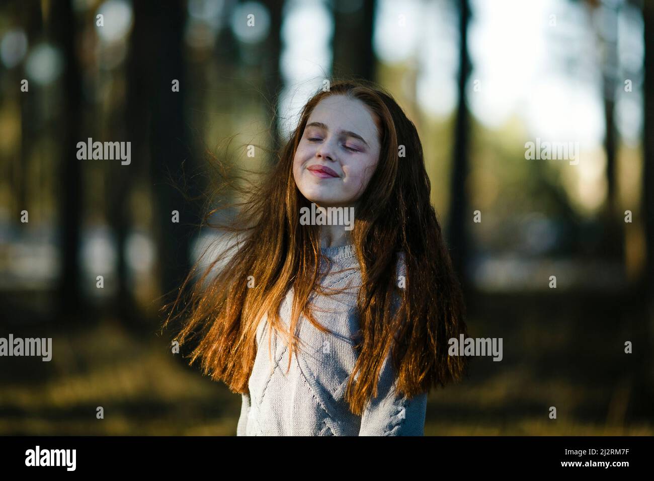 A golden-haired teenage girl enjoying the sun in the summer woods. Stock Photo