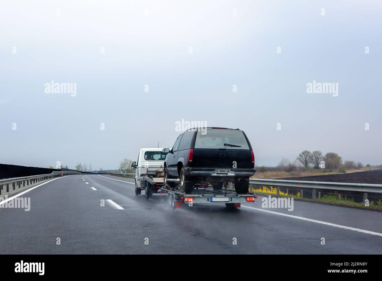 Car carrier trailer with car on wet road. Spray from under the wheels