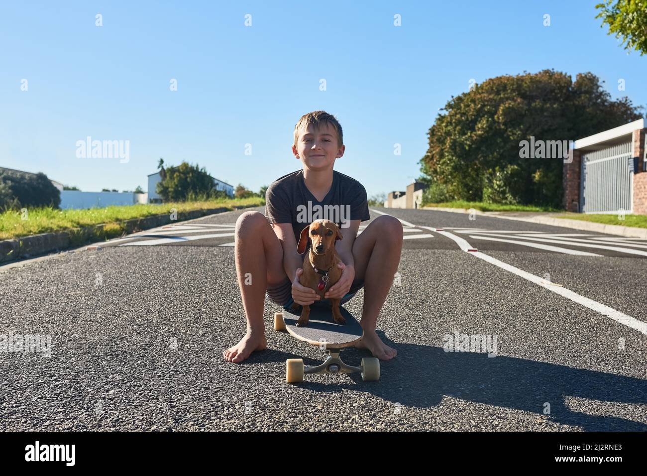 Teaching my dog has to skate. Full length portrait of a young boy and his dog sitting on a longboard. Stock Photo