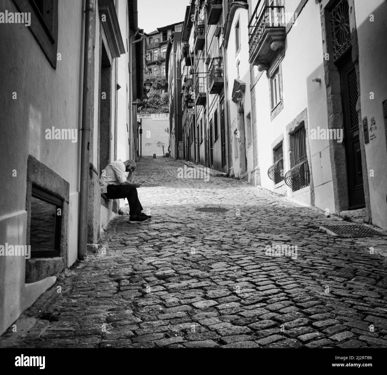Porto, Portugal. March 2022.  A man rests sitting on the step of his house in a narrow street in the historic center of the city Stock Photo