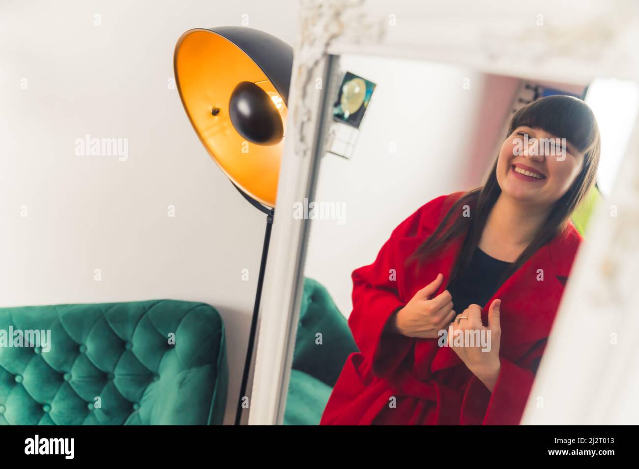 Young European woman trying on red coat. looking at the mirror and smiling online shopping concept portrait copy space . High quality photo Stock Photo