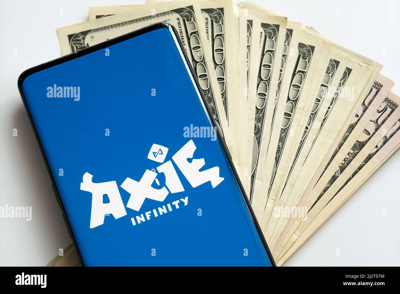 Axie infinity NFT game logo seen on the screen of smartphone and dollar banknotes. Selective focus. Concept. Stafford, United Kingdom, April 3, 2022. Stock Photo