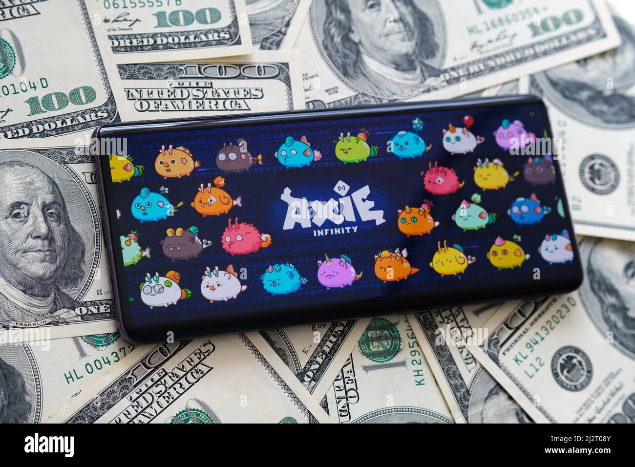 Axie infinity NFT game logo seen on the screen of smartphone and dollar banknotes. Selective focus. Concept. Stafford, United Kingdom, April 3, 2022. Stock Photo