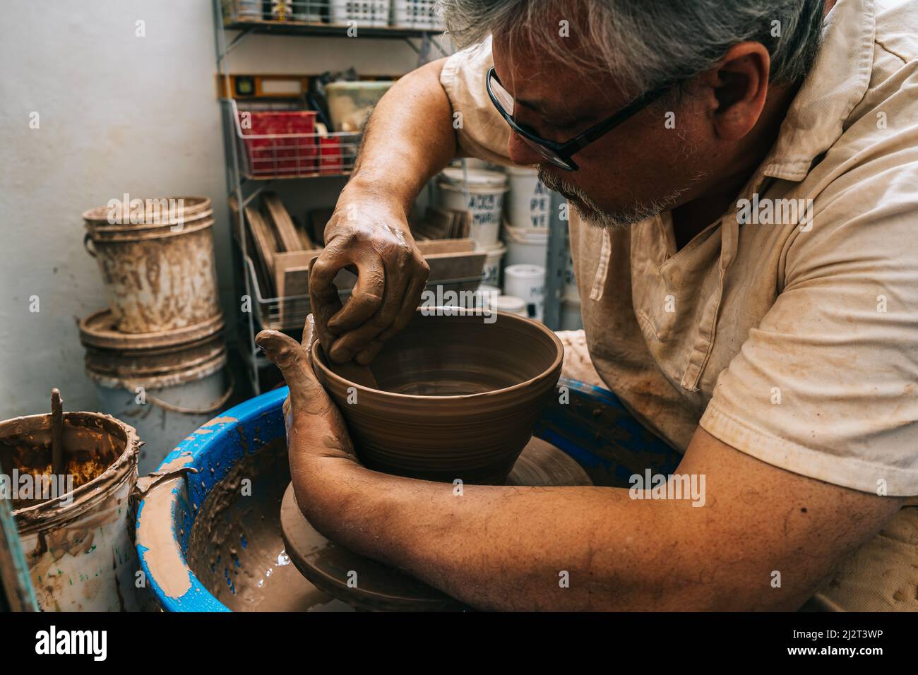 A skilled potter working the clay with his hands on a potter's wheel ...