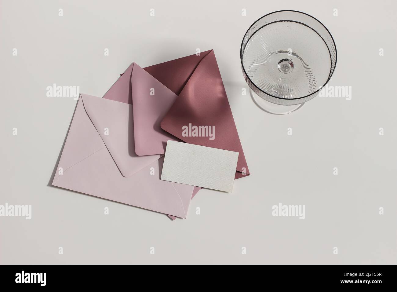 Wedding stationery still life. Champagne, cocktail glass, long shadows. Blush pink , crimson envelopes. Blank business card mock up. Soft beige table Stock Photo