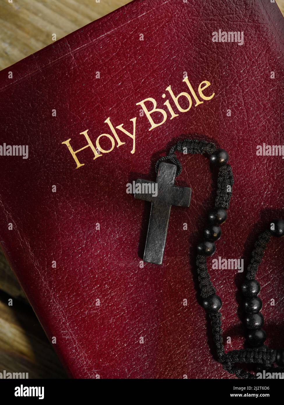 Against the background of a red book with golden letters - the Holy Bible - there are rosaries with a cross. Close-up. There are no people in the phot Stock Photo
