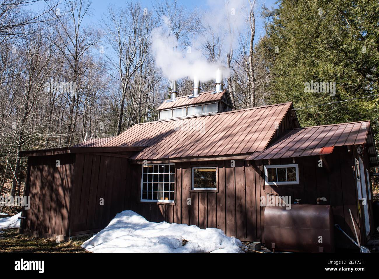 A maple syrup sugar house manufacturing building with steam rising from the chimney in the Adirondack Mountains, NY USA Stock Photo
