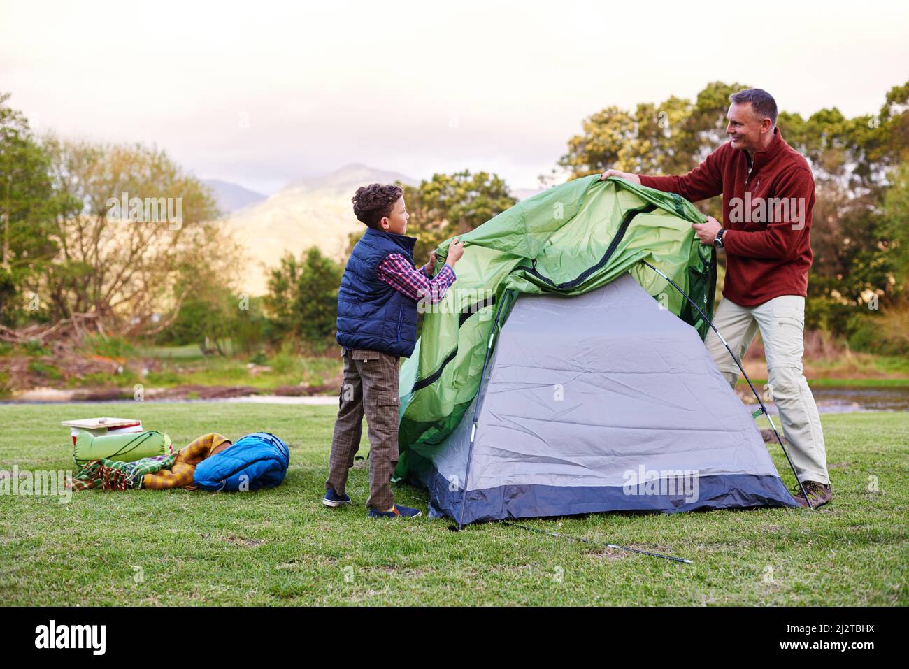 Camp is almost ready. Shot of a father and son setting up a tent together while camping. Stock Photo