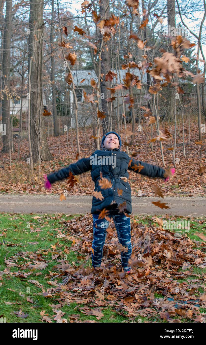 Young teen takes a break from raking leaves, to play in her big pile Stock Photo