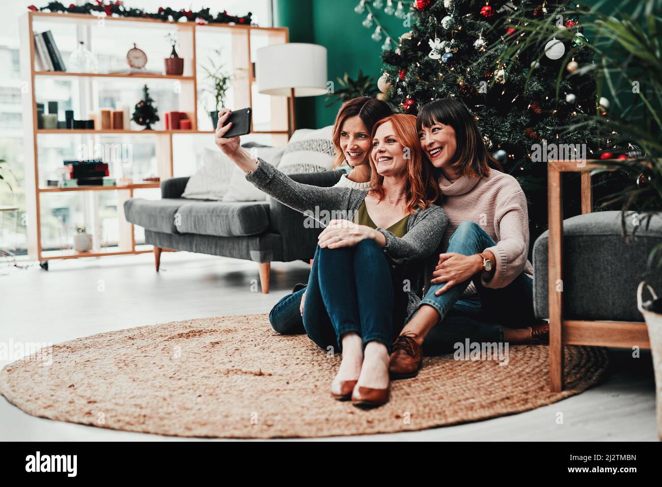 Time for a selfie together. Shot of three attractive middle aged women taking self portraits together with a cellphone at home during Christmas time. Stock Photo