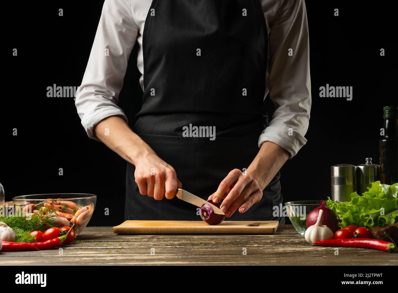 Professional chef cuts red onions for shrimp with vegetables, the ...