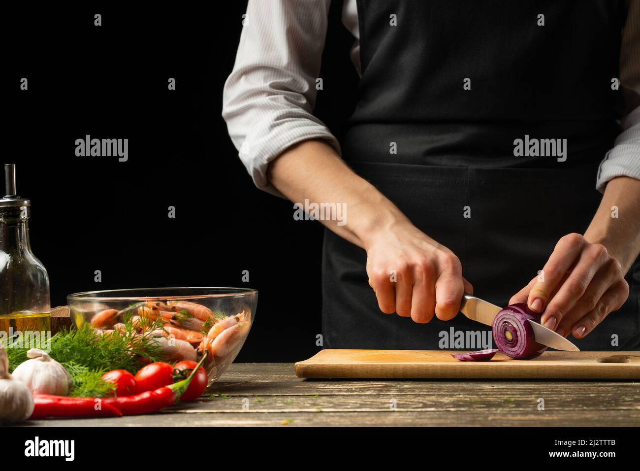 Professional chef cuts red onions for shrimp with vegetables, the ...