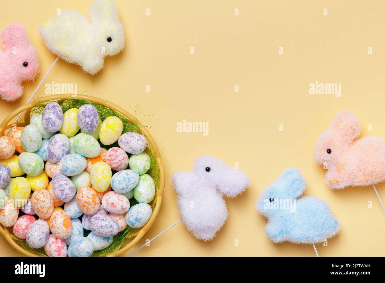 Easter composition of eggs in a basket of toy rabbits on a yellow background with a place for text. Stock Photo