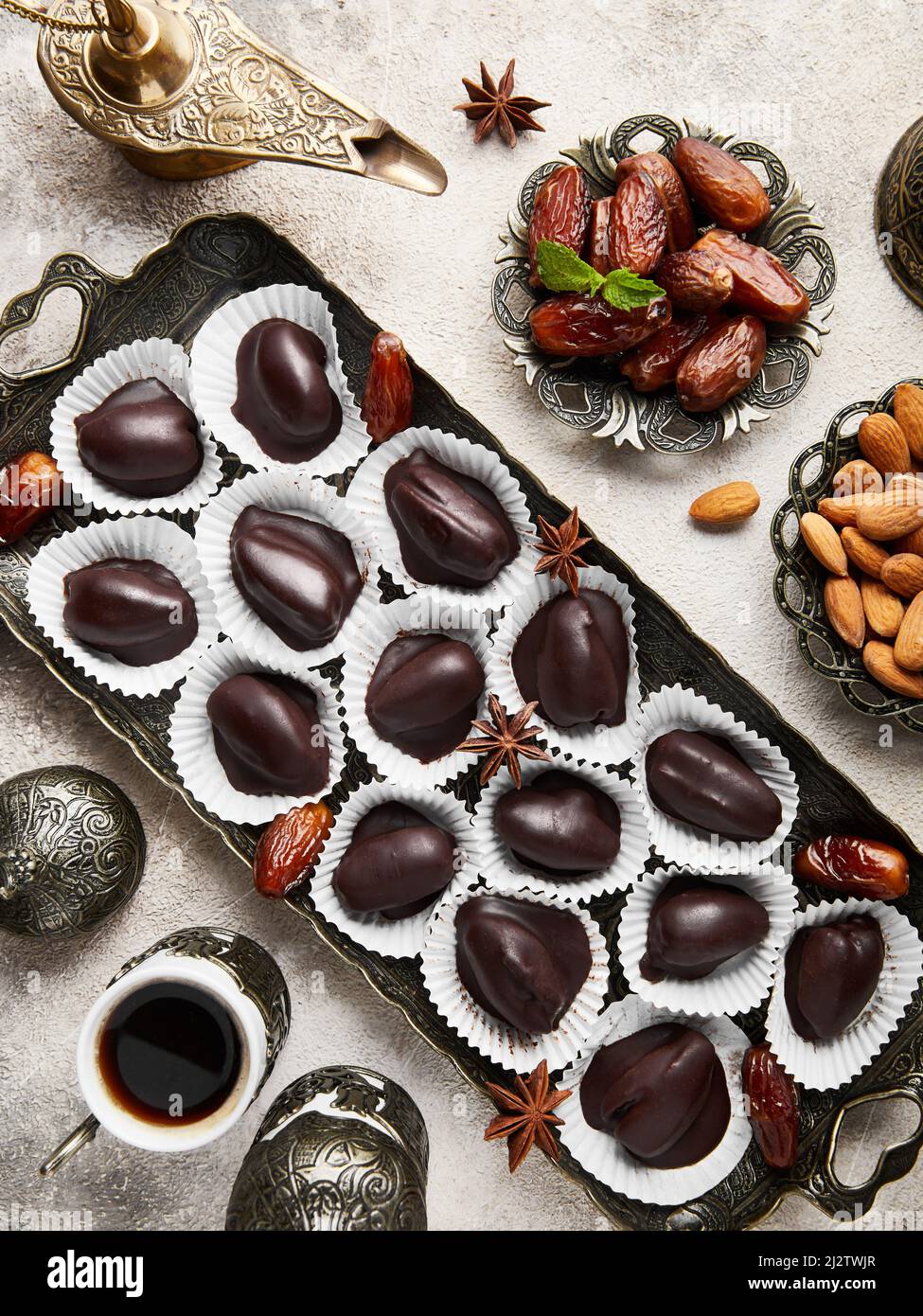 Black Turkish coffee with spices in oriental small cups and Healthy Sugar free Homemade Raw vegan chocolate candies with dried dated and almonds on be Stock Photo