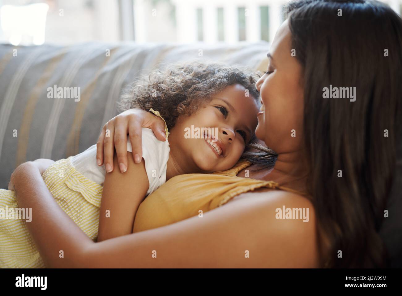 Cherishing these moments with her. Shot of an adorable young girl lying down with her mother on the sofa at home. Stock Photo