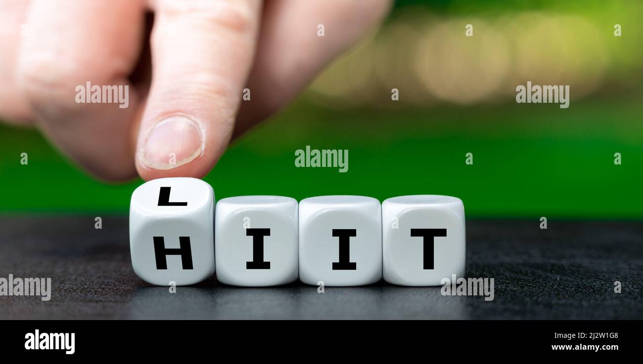 Doing high-intensity interval training (HIIT) or low-intensity interval training (LIIT)? Hand turns dice and changes the expression from HIIT to LIIT. Stock Photo