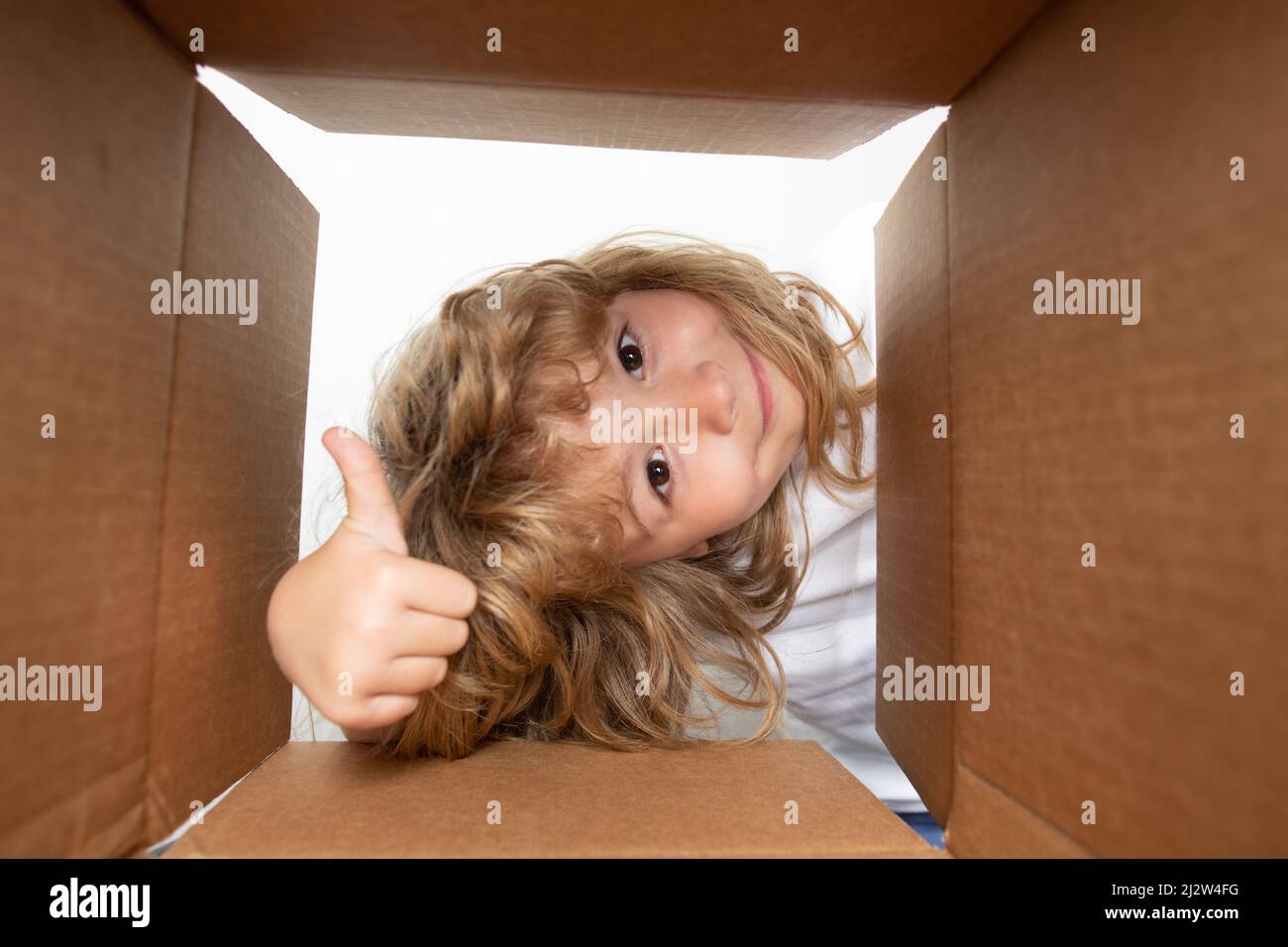 Surprised child boy with thumb up unpacking, opening carton box and looking inside. The package, delivery, surprise, gift for kid. Children emotions Stock Photo