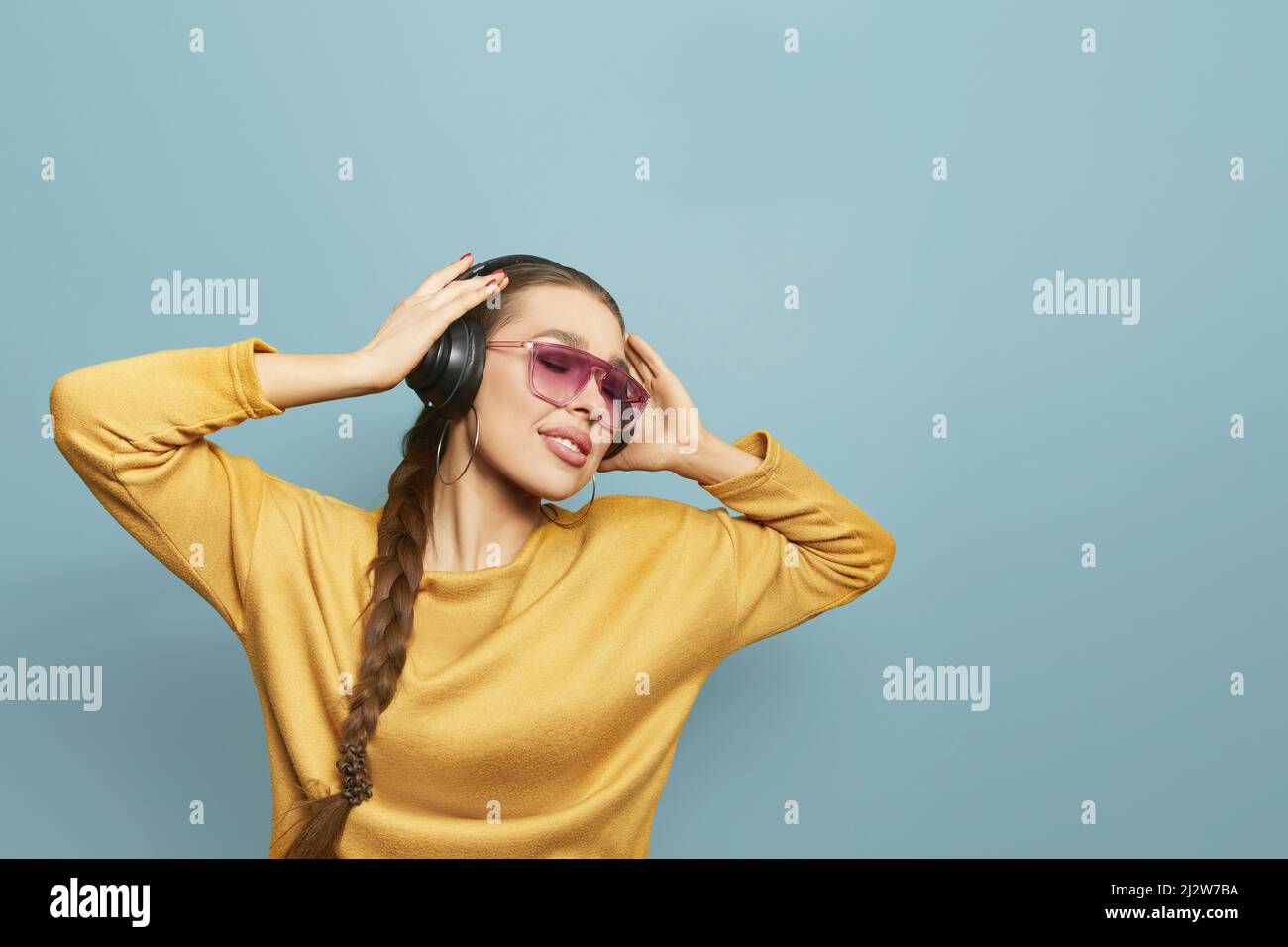 Beautiful woman with sunglasses in yellow sweater listening music with wireless headphones. Girl uses wireless earphones and dancing. Stock Photo