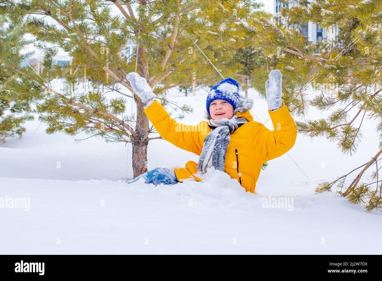 in a bright yellow jacket and a blue hat, a boy in the snow Stock Photo